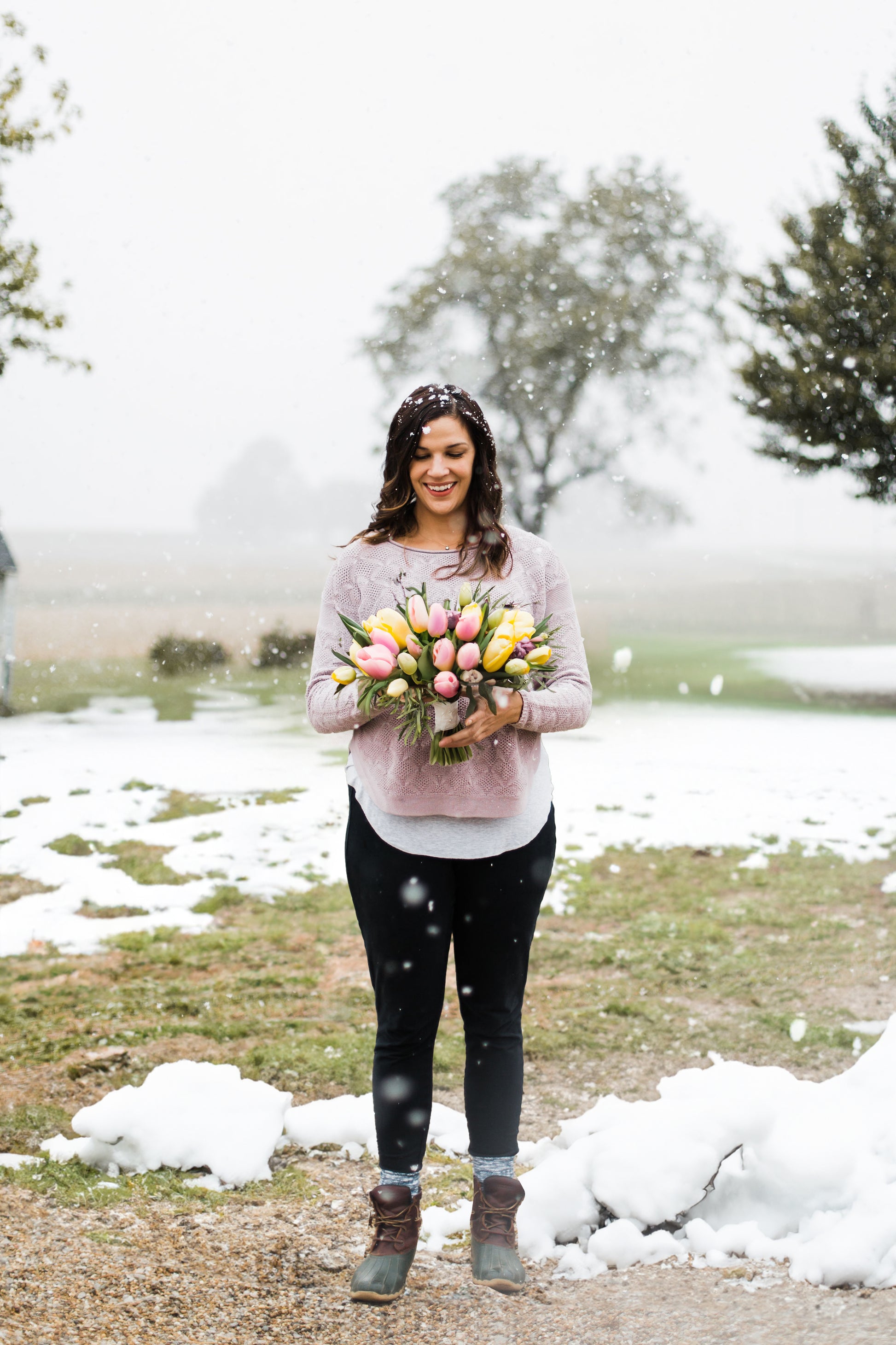 A woman holding a bouquet of tulips with snow falling.