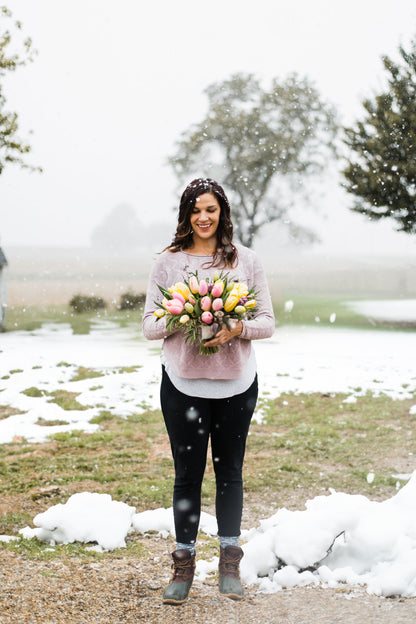 A woman holding a bouquet of tulips with snow falling.