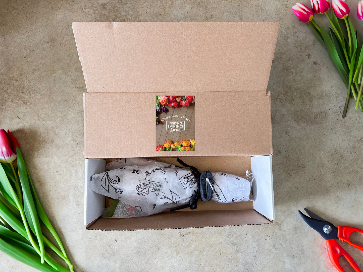 A box of tulips that has been delivered to a doorstep, with the tulips themselves displayed outside of the box.